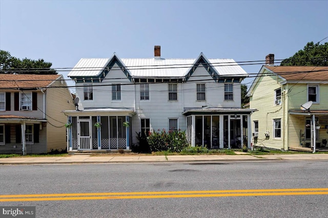 view of front of house with a sunroom, a chimney, and metal roof