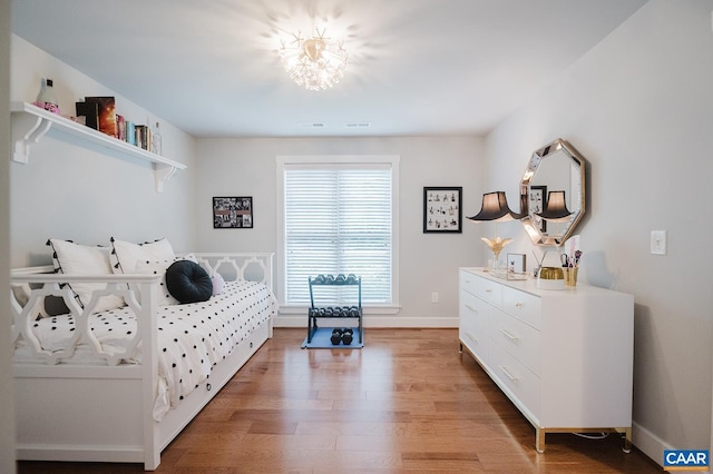 bedroom with baseboards, an inviting chandelier, and light wood-style floors
