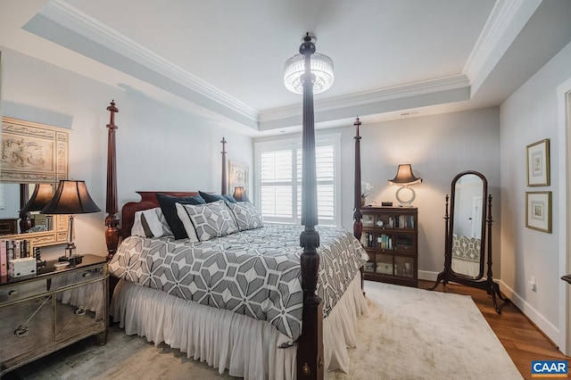 bedroom with baseboards, crown molding, wood finished floors, and a tray ceiling