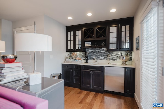 bar featuring light wood finished floors, a sink, recessed lighting, backsplash, and indoor wet bar