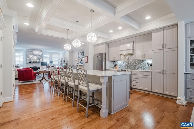 kitchen featuring custom exhaust hood, a breakfast bar, stainless steel appliances, light wood finished floors, and gray cabinetry