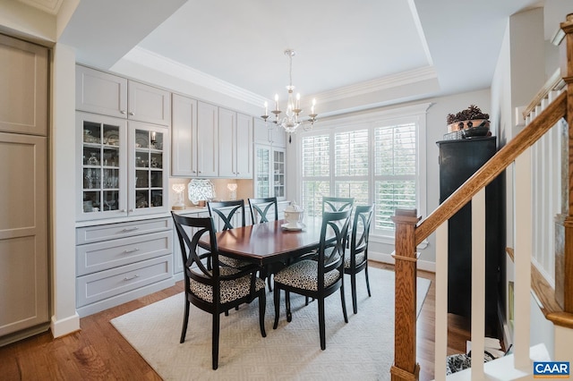 dining space with a tray ceiling, a chandelier, wood finished floors, stairway, and ornamental molding