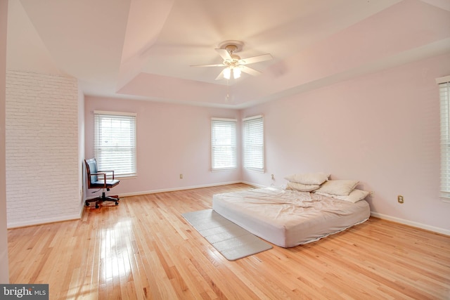 bedroom with a ceiling fan, baseboards, a raised ceiling, and hardwood / wood-style floors