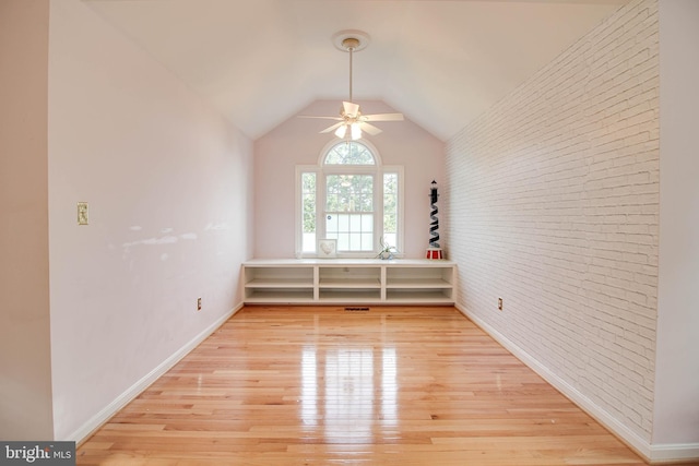 empty room featuring light wood-style floors, brick wall, a ceiling fan, baseboards, and lofted ceiling