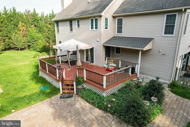 back of property with a shingled roof, a deck, a chimney, a patio, and a yard