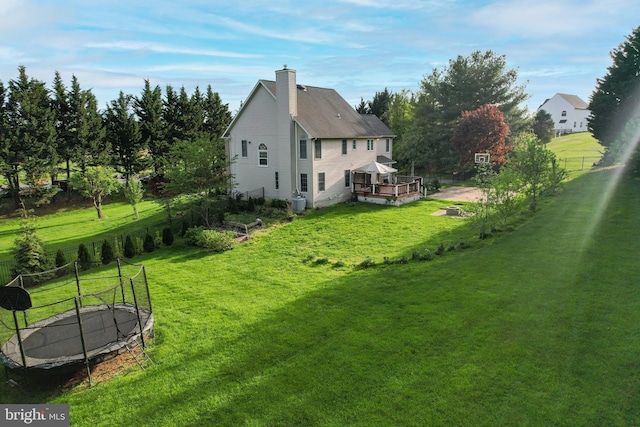 view of yard featuring a deck, fence, and a trampoline