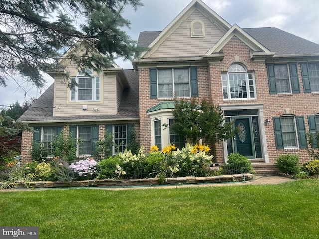 view of front of house featuring brick siding, a shingled roof, and a front yard