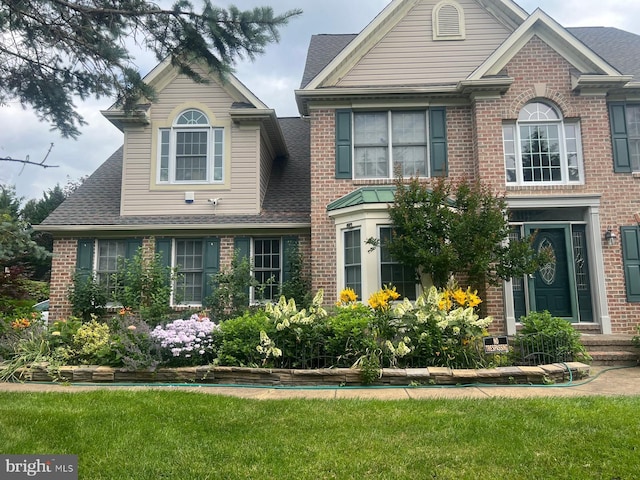 view of front of home with brick siding, a shingled roof, and a front yard