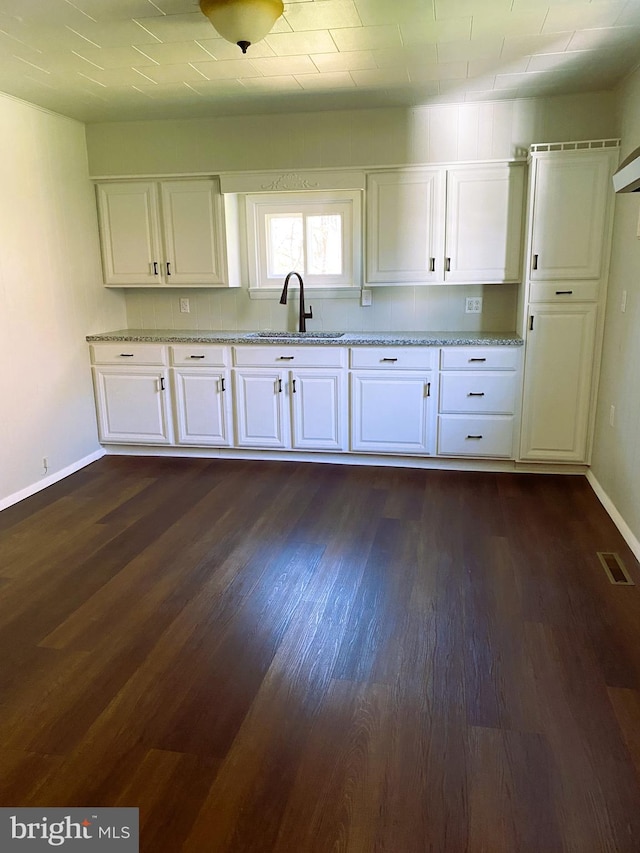 kitchen featuring white cabinets, dark wood-style floors, visible vents, a sink, and baseboards
