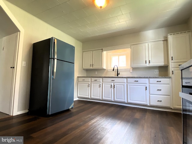 kitchen featuring white cabinets, a sink, dark wood-style flooring, freestanding refrigerator, and light stone counters