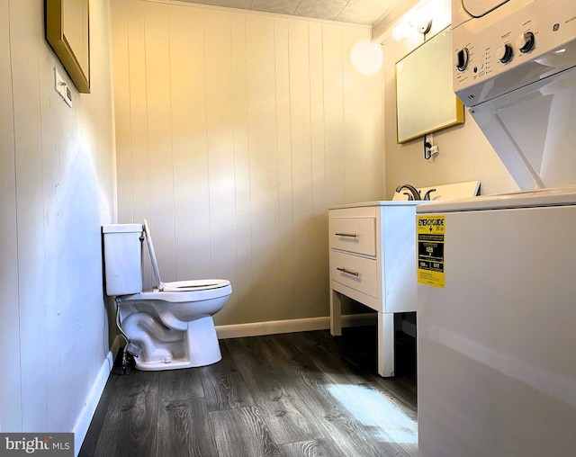 bathroom featuring stacked washer and dryer, baseboards, wood finished floors, and toilet
