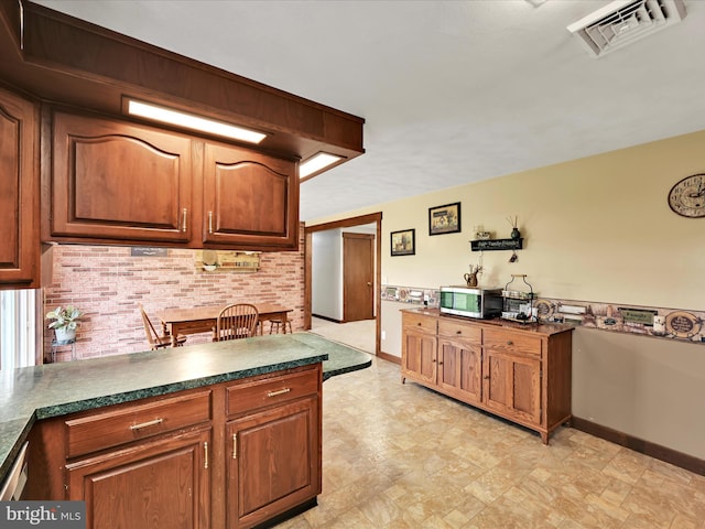 kitchen featuring dark countertops, brown cabinetry, stainless steel microwave, baseboards, and visible vents