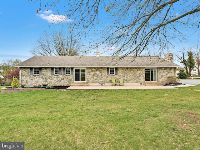 back of house featuring a chimney, a lawn, stone siding, a shingled roof, and a patio