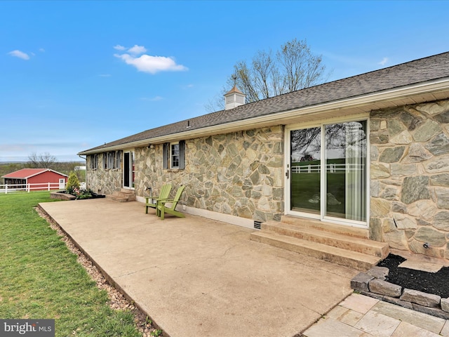 back of house featuring stone siding, a patio area, a chimney, and entry steps
