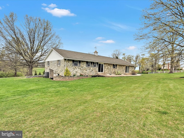 single story home featuring stone siding, a chimney, a front yard, and cooling unit