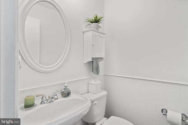 half bathroom with a sink, a wainscoted wall, and toilet