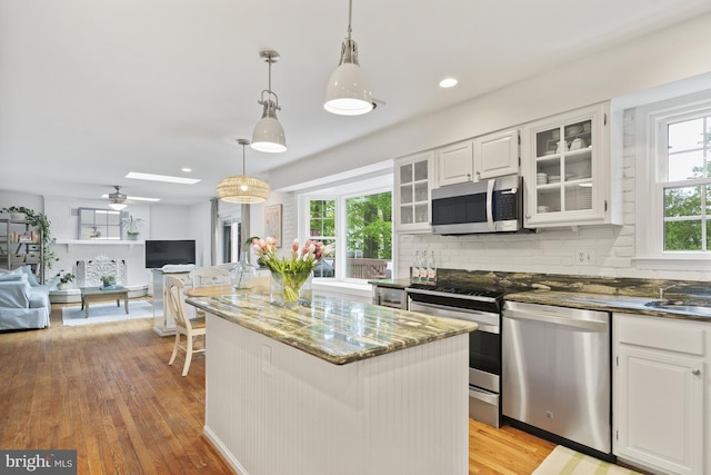 kitchen featuring dark stone counters, appliances with stainless steel finishes, light wood finished floors, and open floor plan