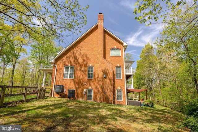 rear view of house featuring fence, a balcony, a chimney, brick siding, and a lawn