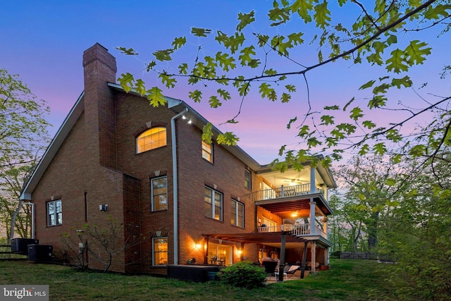 back of house at dusk with a chimney, a patio area, brick siding, and a balcony