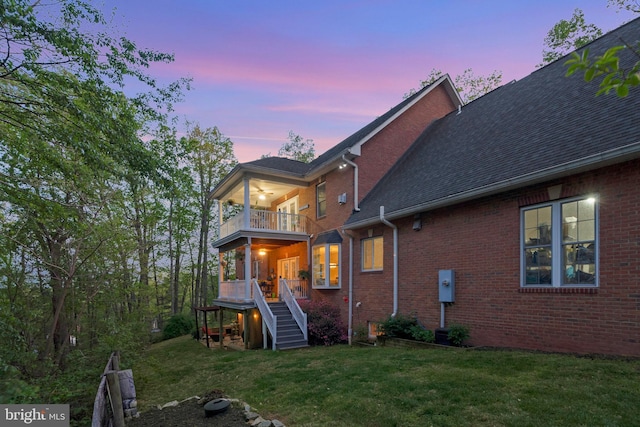 back of property featuring a lawn, brick siding, a balcony, and stairs