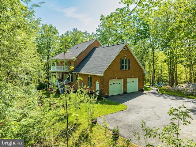 view of home's exterior featuring a shingled roof, brick siding, a garage, a balcony, and driveway
