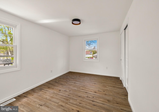unfurnished bedroom with wood finished floors, visible vents, baseboards, and multiple windows