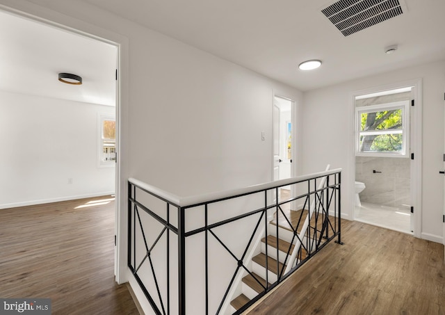 hall featuring baseboards, wood finished floors, visible vents, and an upstairs landing