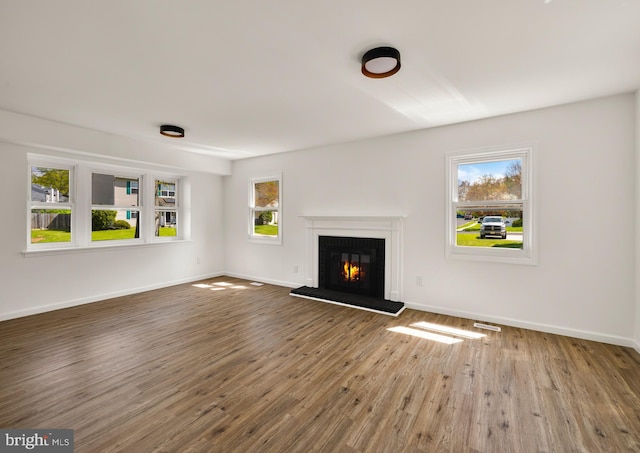 unfurnished living room with a glass covered fireplace, wood finished floors, visible vents, and baseboards
