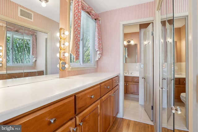 bathroom with wallpapered walls, vanity, healthy amount of natural light, toilet, and wood finished floors