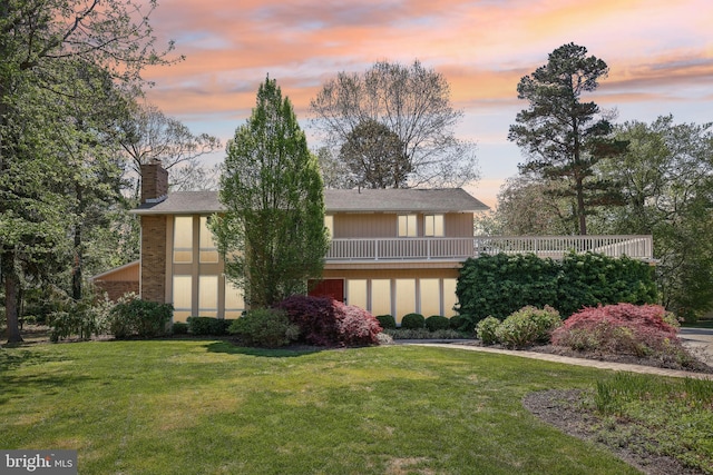 back of house featuring a yard, a chimney, brick siding, and a balcony