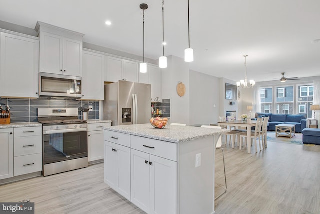 kitchen featuring light wood-style floors, open floor plan, tasteful backsplash, ceiling fan with notable chandelier, and stainless steel appliances