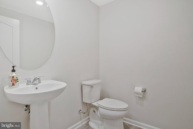 half bath with toilet, baseboards, and wood finished floors