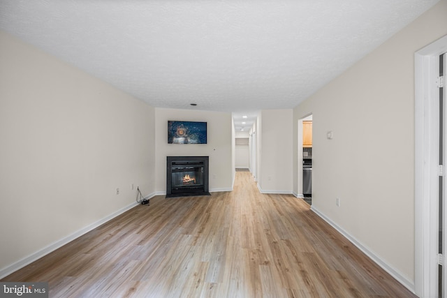unfurnished living room featuring light wood finished floors, a textured ceiling, baseboards, and a fireplace with flush hearth