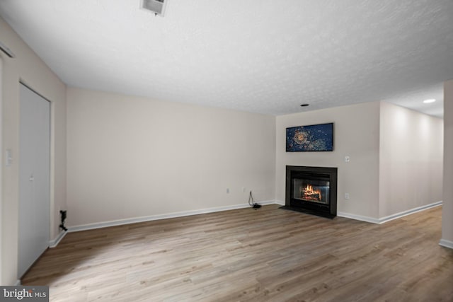 unfurnished living room featuring wood finished floors, a fireplace with flush hearth, a textured ceiling, visible vents, and baseboards