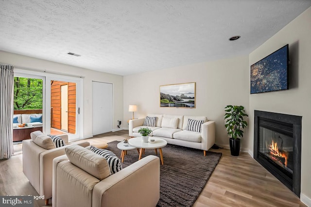 living area featuring a textured ceiling, light wood-style floors, baseboards, and a glass covered fireplace