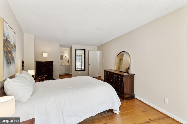 bedroom with light wood-style floors, baseboards, and connected bathroom