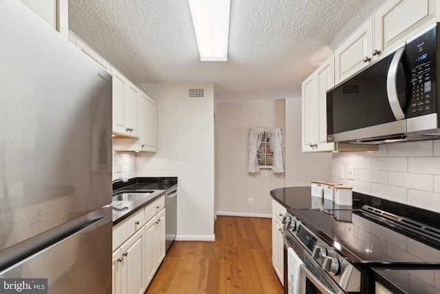 kitchen with dark countertops, appliances with stainless steel finishes, a sink, light wood finished floors, and decorative backsplash