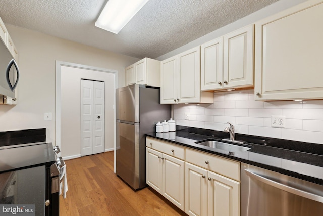 kitchen featuring a textured ceiling, appliances with stainless steel finishes, tasteful backsplash, a sink, and light wood-style floors