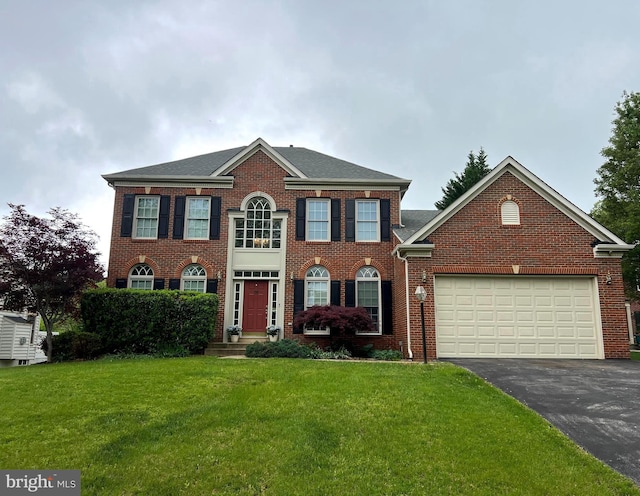 colonial house featuring aphalt driveway, a garage, brick siding, and a front yard