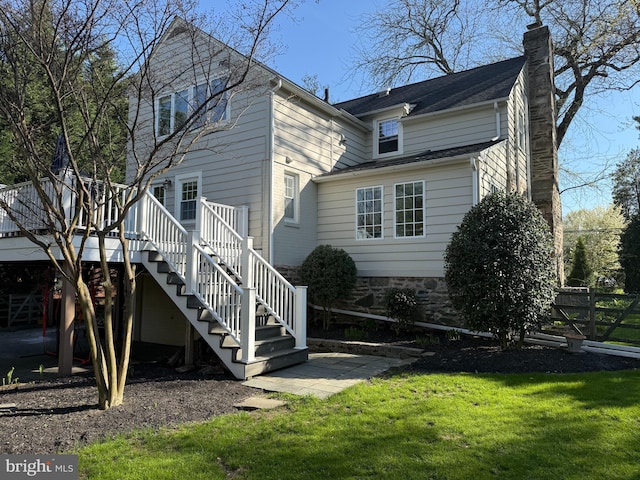back of house featuring a lawn, stairs, a wooden deck, and a chimney