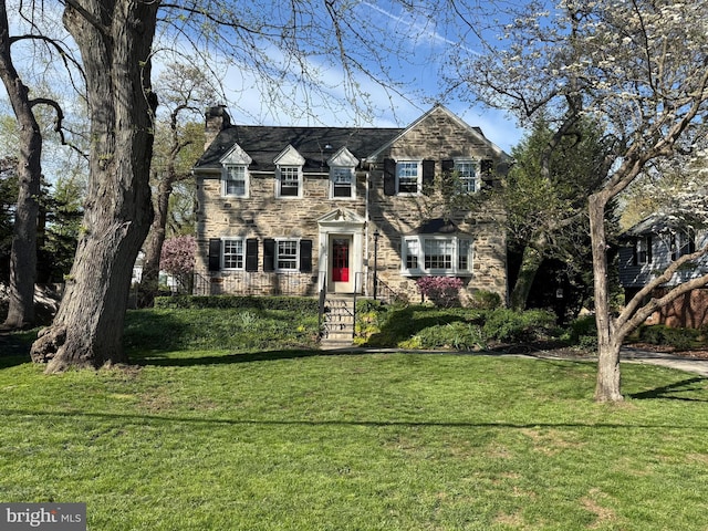 view of front of property with a chimney, a front yard, and stone siding