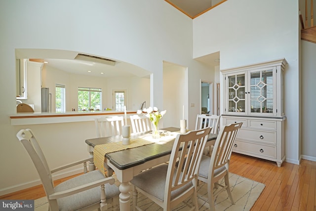 dining area featuring arched walkways, a towering ceiling, light wood-style floors, and baseboards