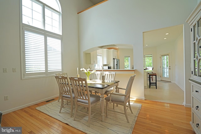 dining area with arched walkways, light wood finished floors, a high ceiling, and baseboards
