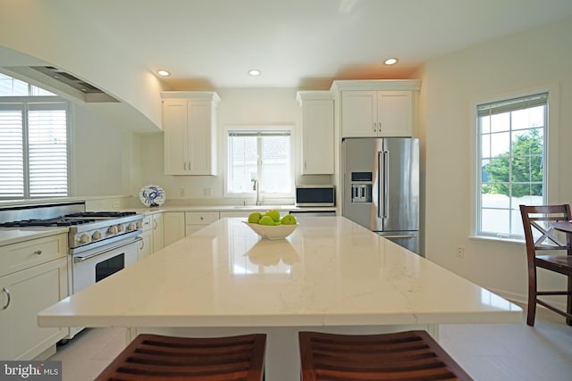 kitchen featuring appliances with stainless steel finishes, a center island, a sink, recessed lighting, and light stone counters