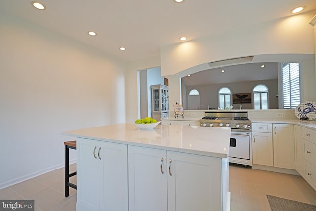 kitchen with gas stove, recessed lighting, arched walkways, white cabinets, and a center island