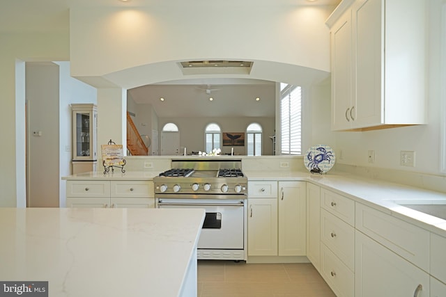 kitchen featuring stainless steel range, arched walkways, white cabinetry, a peninsula, and light stone countertops
