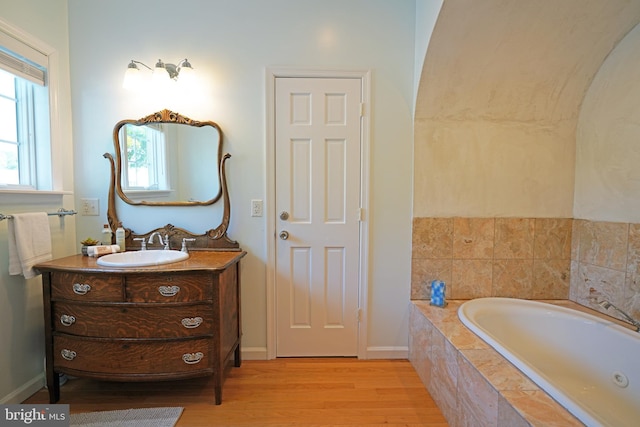 full bath featuring wood finished floors, vanity, a garden tub, and baseboards