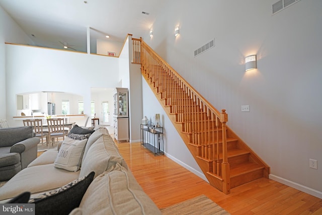 living area with wood finished floors, ceiling fan, stairway, baseboards, and a high ceiling