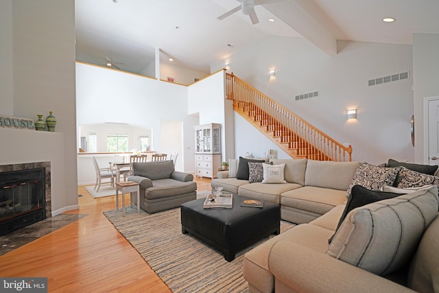 living area with ceiling fan, high vaulted ceiling, stairway, wood finished floors, and a tile fireplace