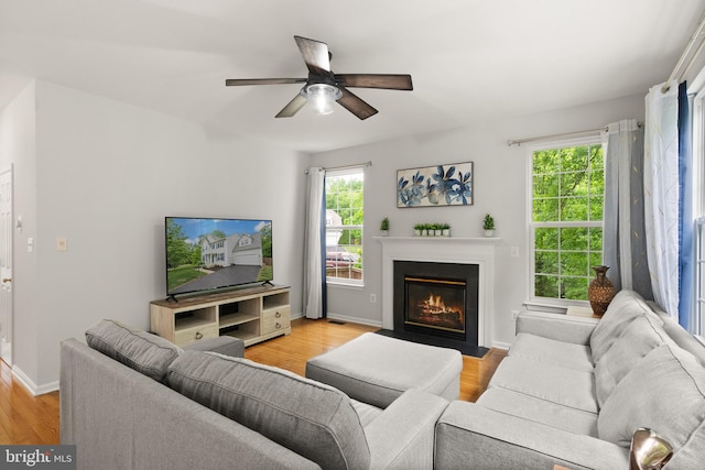 living room with a ceiling fan, baseboards, light wood-type flooring, and a fireplace with flush hearth
